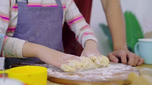 Asian girl kneading dough with flour on wooden board with parents assisting.