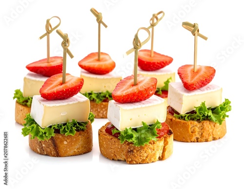 A neatly arranged group of toasted bread appetizers with cheese, lettuce, and strawberries on toothpicks