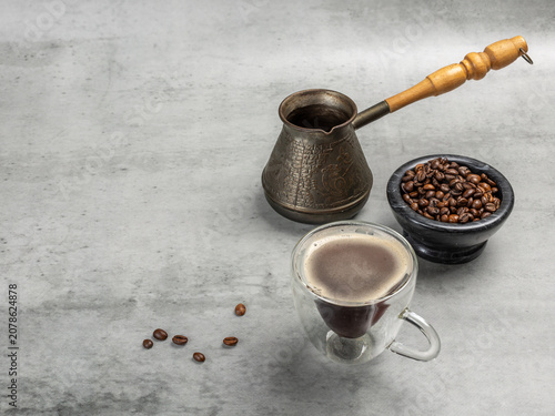 Cup of coffee, a stone bowl with roasted coffee beans and a cezve.