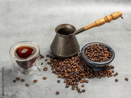 Cup of coffee, a cezve and a stone bowl with roasted coffee beans.