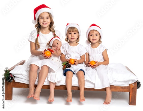 Three children in Santa hats sitting on a bed