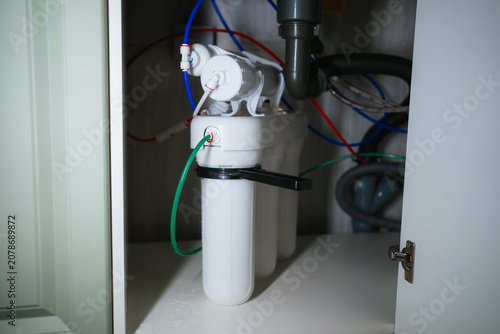 Reverse osmosis water purification system with visible filter cartridges and a network of colored tubing installed under a kitchen sink, providing filtered and clean drinking water