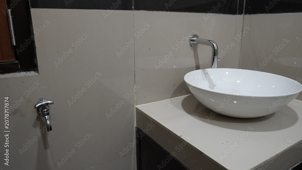 Fototapeta premium Minimalist bathroom sink with sleek chrome faucet. White basin rests on clean, light-toned countertop. Dark-tiled wall contrasts with soft, neutral tones