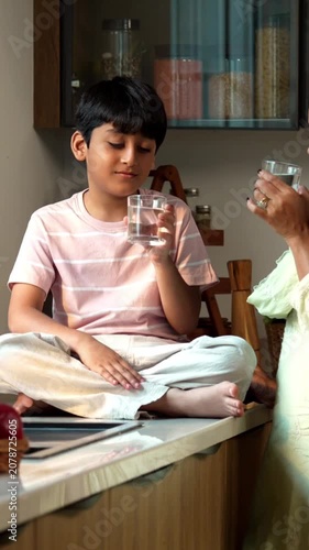 Indian kid drinking water from glass with young mother in modern kitchen, spending quality time together indoors at home in everyday routine, healthy lifestyle parent child bonding video clip