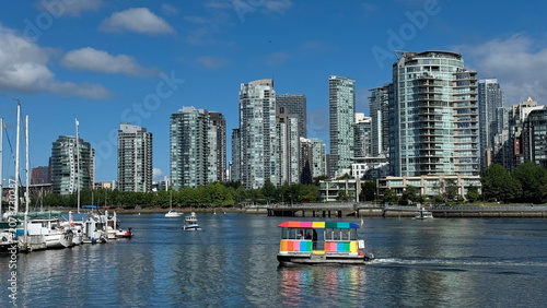 A signature rainbow-striped Aquabus water ferry carries passengers across the blue waters of False Creek on a beautiful clear day.