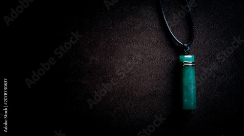 A slender green jade pendant shaped like a silique on a dark background.
