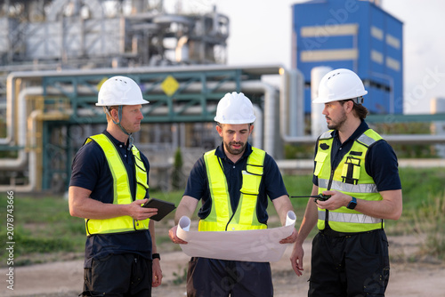 Engineers discussing blueprint planning refinery construction project