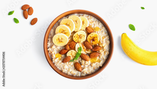 Overhead view of a wooden bowl of oatmeal with banana, almonds, honey, and fresh mint
