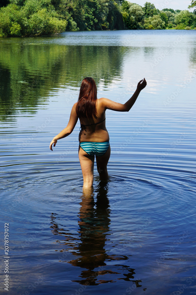 Fototapeta premium real woman wading into a calm lake water causing ripples before enjoying a refreshing summer swim