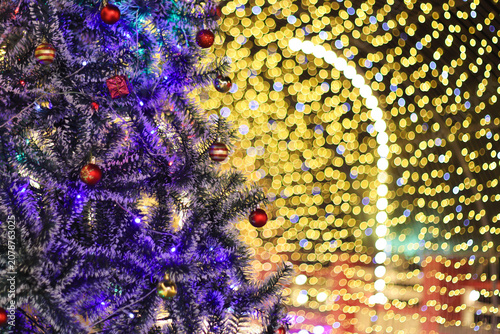 Christmas tree with purple lights next to a bright golden bokeh background wall at a night festival