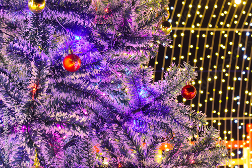 Christmas tree branches closeup with bright red ornaments and sparkling gold bokeh background lights