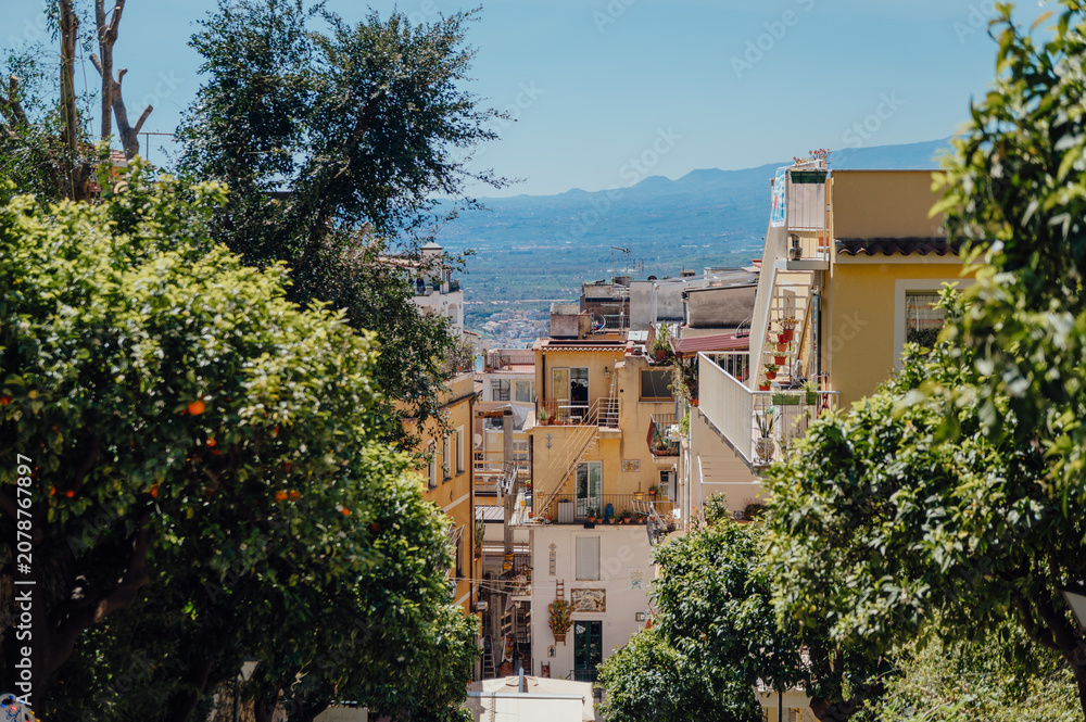 Fototapeta premium Lush trees framing a sunny hillside Italian town Taormina