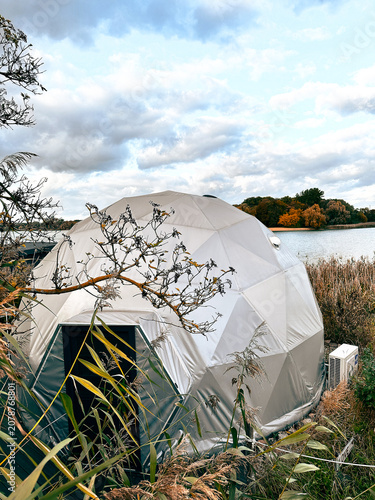 Geodesic dome tent by the lake surrounded by autumn foliage  