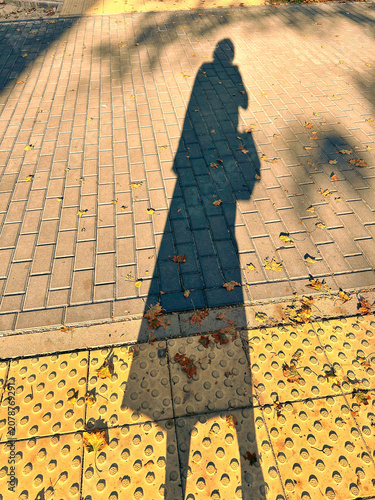 Shadow of a person walking on pavement with autumn leaves around - Concept of autumn depression  