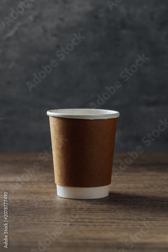 Brown Paper Coffee Cup on Wood Surface Against Dark Background