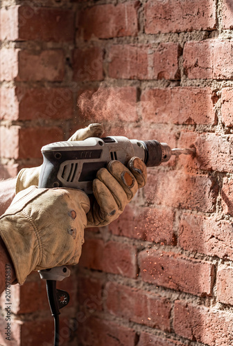 Construction worker drilling into red brick wall with electric power tool