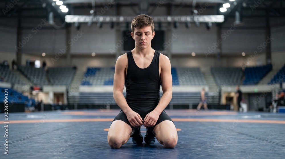 Fototapeta premium Young male wrestler sitting on mat in gymnasium preparing for match 