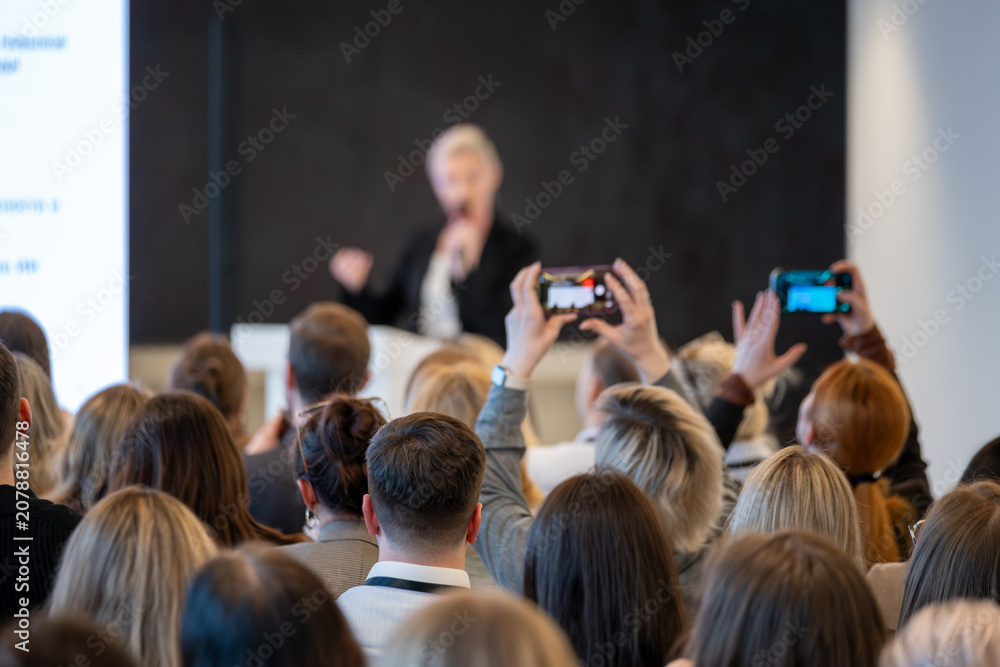 Obraz premium Crowd of attendees record presenter at conference, smartphones held high, focus on audience engagement and live documentation.