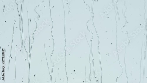 Rain streaks and water droplets on glass window create minimal blue background, abstract texture, soft calm mood.