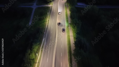 Aerial view of cars driving on a well-lit road at night, showcasing the continuous movement and interaction of vehicles in a serene urban environment