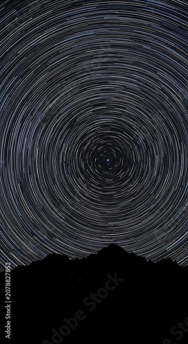 Starry Night Sky Over Mountain Landscape with Circular Star Trails.