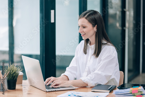 Smiling young woman working on laptop in modern bright office interior