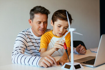 Father and son with laptop assembling wind turbine model