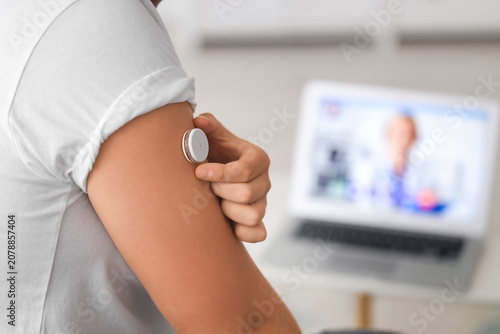 Diabetic young man with glucose sensor receiving online consultation from doc...