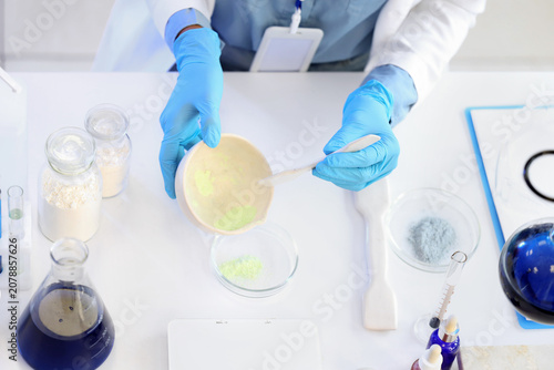 Young female chemist with mortar and Petri dish working in lab, closeup