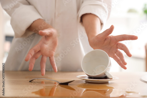 Photos Woman spilling coffee from cup on table in kitchen, closeup