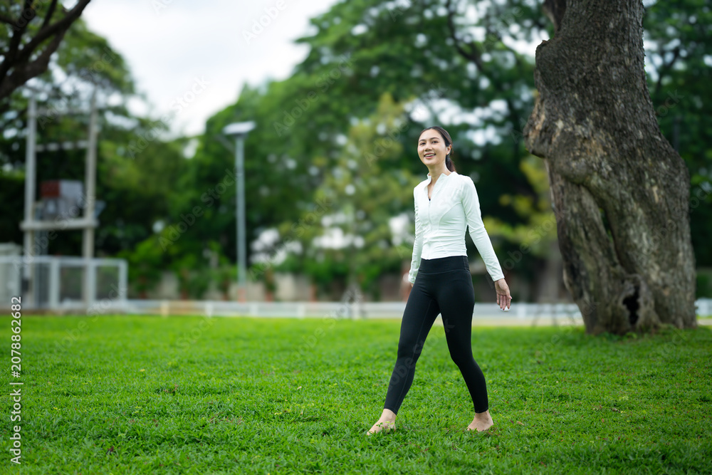 Fototapeta premium Young Woman Walking Barefoot on Green Grass in Park for Grounding and Earthing Wellness Practice