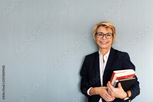 Portrait of mature businesswoman standing at a wall holding stack of books