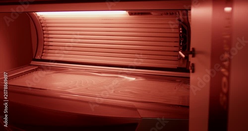 Interior view of a closed tanning bed with illuminated red light lamps inside