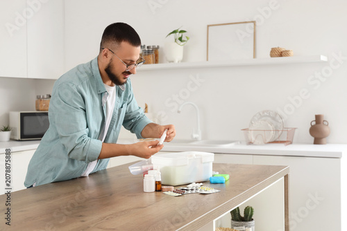 Young man taking lancet pen from first aid kit at table in kitchen