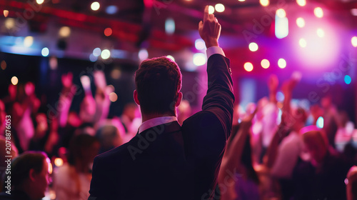 Rear view of a young adult man in a suit raising his hand at a crowded auction or gala event with vibrant cinematic lighting