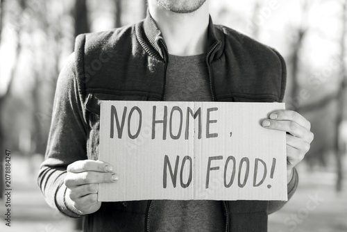 Homeless man holding cardboard with text NO HOME NO FOOD in park, closeup