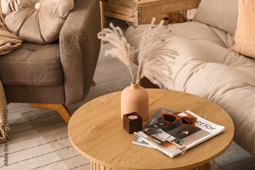 Vase with dry reeds, sunglasses and magazines on table in living room