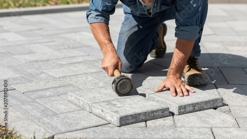 A skilled worker carefully installs a new patio using paving stones and a rubber mallet. This home improvement project showcases the precision involved in outdoor paver installation