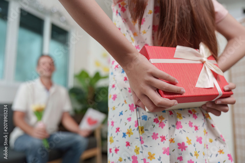 Daughter hiding surprise Father's Day gift behind back for dad at home