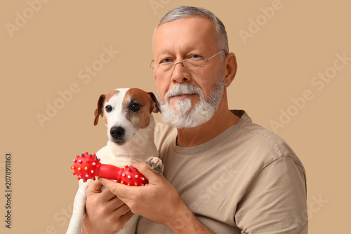 Middle-aged man with cute dog and toy on beige background