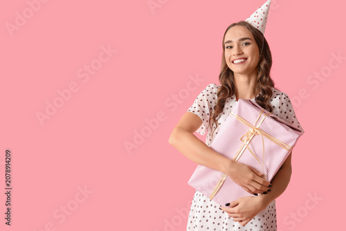 Happy young woman in party hat with gift box celebrating Birthday on pink bac...