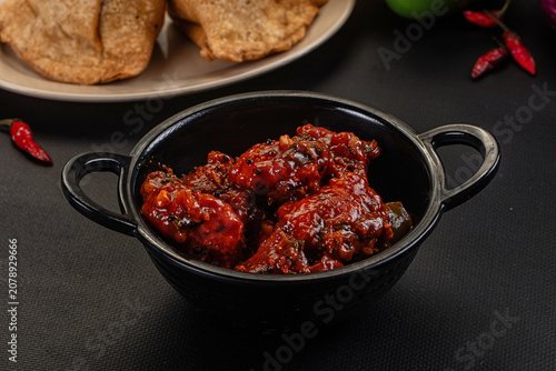 Tableau sur toile Spicy chicken curry in black bowl with fried bread and red chilies on dark backg