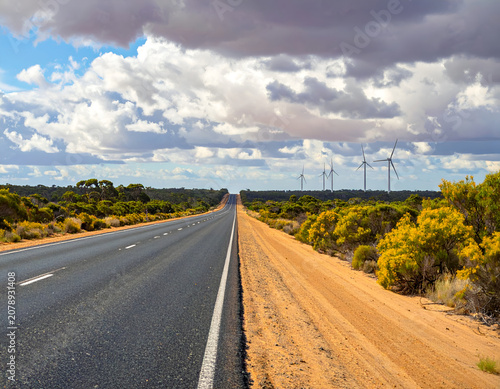Long Straight Road Through Arid Landscape Towards Wind Turbines Under Dramatic Sky.