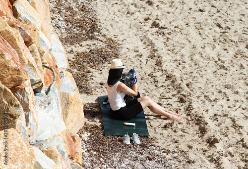 Fotografie Mujer en arena playa con sombrero, crema solar , zapatillas, toalla, ropa y prot