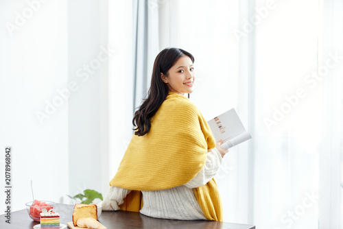 Foto Smiling young woman reading at home in soft morning light with yellow shawl