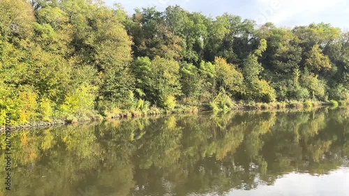 idyllic river landscape seen from a boat in autumn, sunny day, blue sky, trees reflected in the river, a calm river, yellow-green leaves on the trees, beautiful green reflection