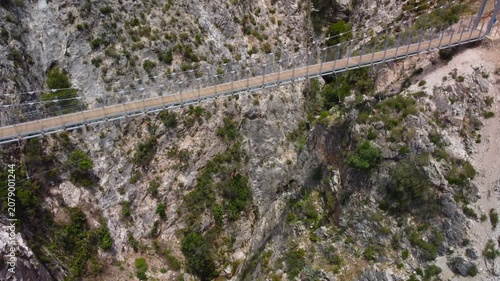 Aerial view of suspension bridge of 'El Saltillo Canillas de Aceituno' in the beautiful mountain landscape of Canillas de Aceituno on a sunny day, Malaga, Spain