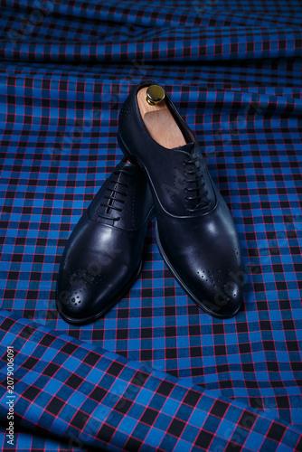 Male black leather shoes on dark blue checkered suit fabric background. Copy space for logo, design, advertising. Accessories for men