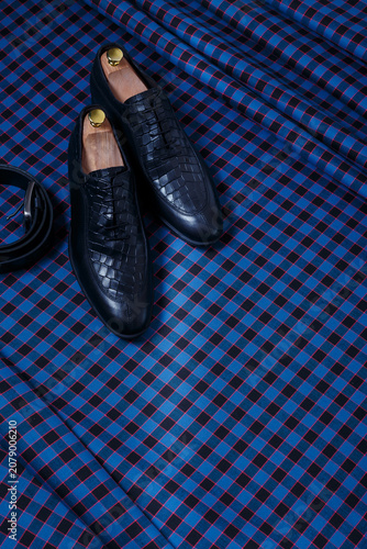 Male black leather shoes and belt on dark blue checkered suit fabric background. Copy space for logo, design, advertising. Classic formal accessories for men