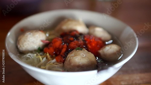 A bowl of traditional Indonesian beef meatballs with noodles, rice vermicelli, savory broth, chili sauce, and sweet soy sauce.